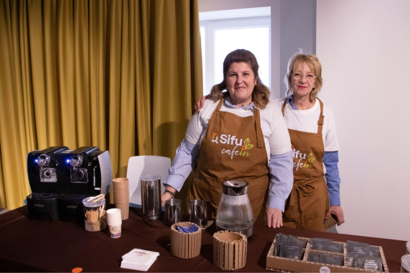 Dos baristas de CafeIn posan frente a una mesa de servicio de café