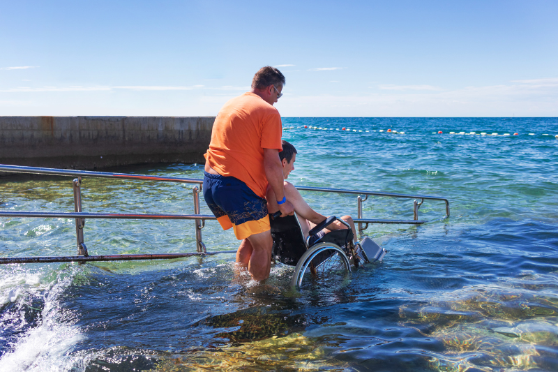 Una persona en silla de ruedas entra en el mar con ayuda de un asistente