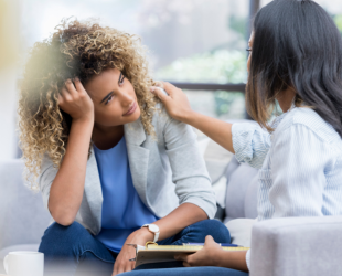 dos mujeres están sentadas hablando, una toca el hombro de la otra en señal de apoyo